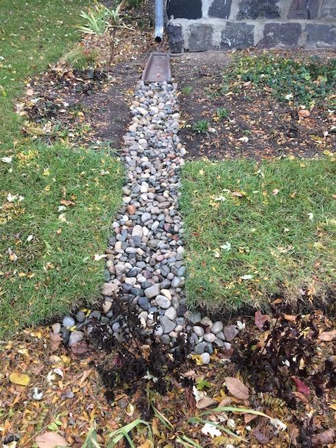 Photo of plastic- and rock-lined trench leading from downspout to the rain garden.